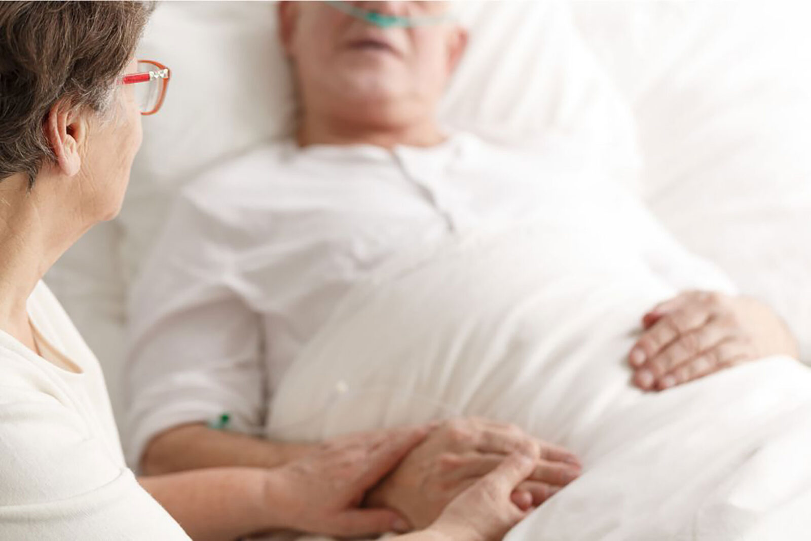 Woman holding hands, caring for a patient in bed.