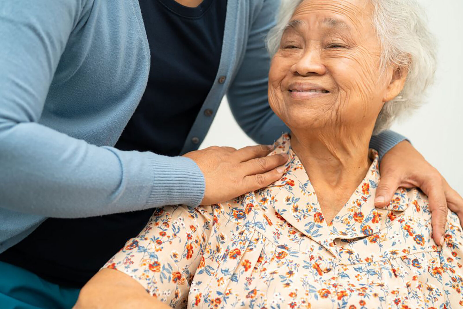 Elderly woman smiling, caregiver comforting her with touch.